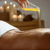 Massage oil being poured onto a person's back in a spa setting with candles.